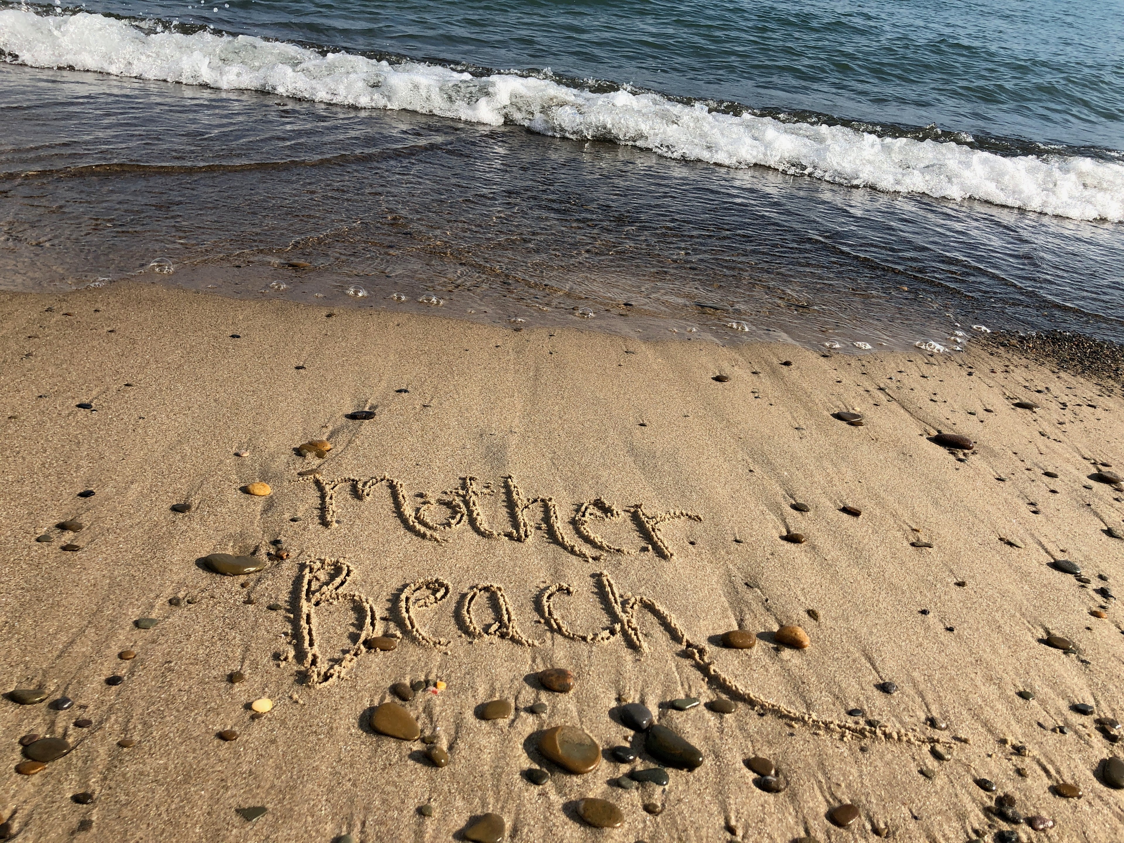 Sand with 'Mother Beach' written on it, waves in the background