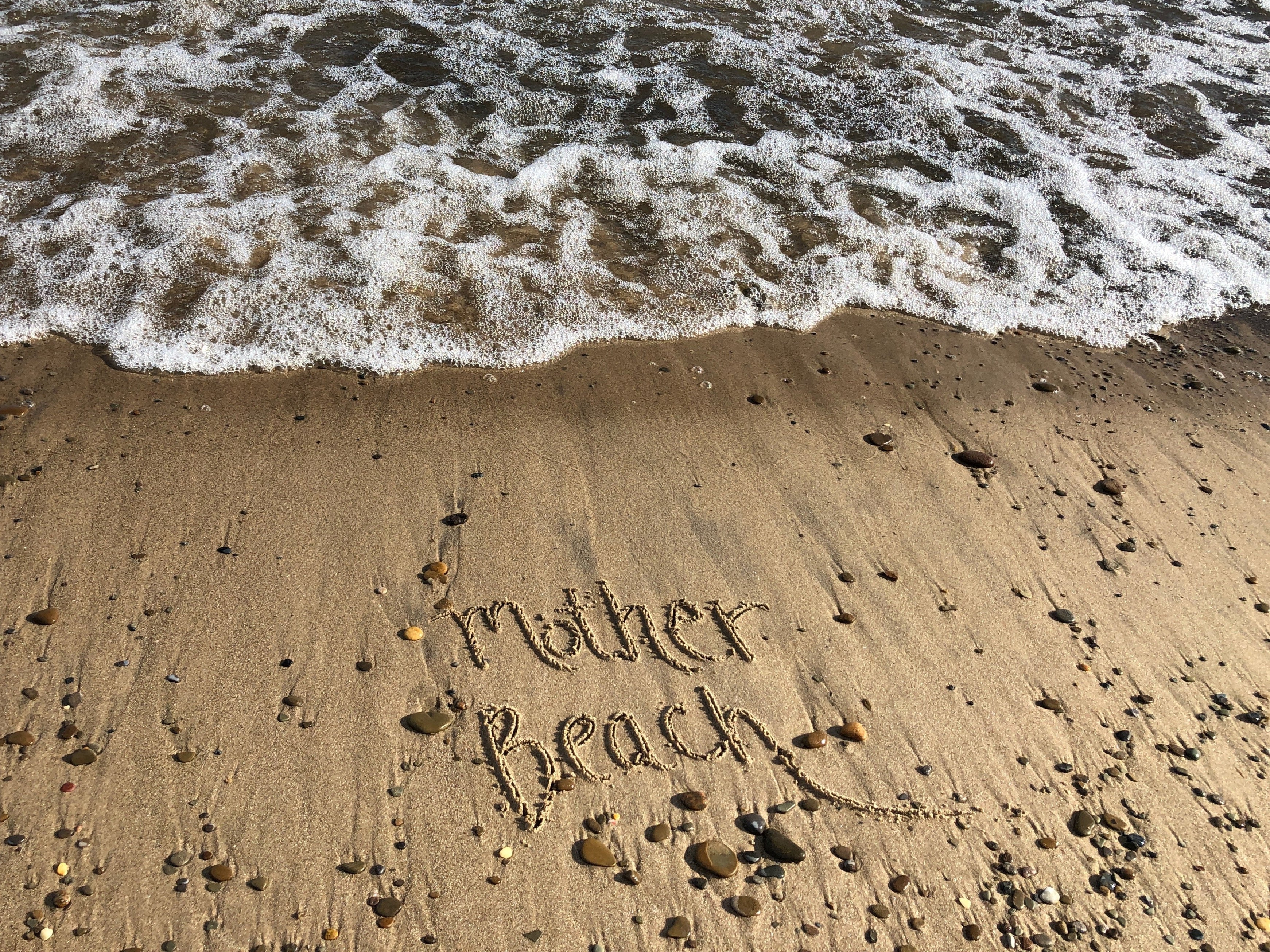 Text 'Mother Beach' written in sand with waves in the background