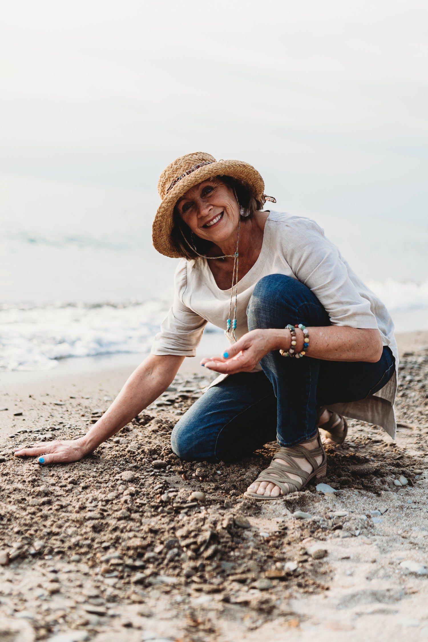 Woman sitting on a beach wearing a hat and smiling.
